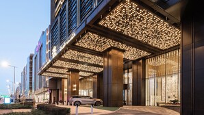 L’entrée moderne d’un hôtel, avec une allée couverte, de grandes fenêtres et une voiture garée à l’extérieur.
