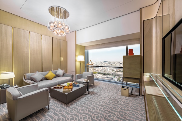 Habitación de hotel moderna con vistas a la ciudad, un sofá, sillones, una mesa de centro y un televisor.