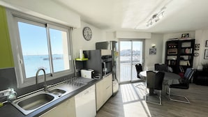 A modern kitchen with a large window, a dining area with a view, and a bookshelf. - Pieds Dans L'eau T3 Top Cosy - Face à la mer (Port-Louis)