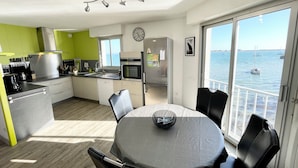 A modern kitchen with a view of the sea, a dining area with a table and chairs, and a large window. - Pieds Dans L'eau T3 Top Cosy - Face à la mer (Port-Louis)