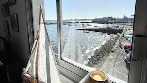 A room with a large window overlooking a beach with boats and a pier. - Pieds Dans L'eau T3 Top Cosy - Face à la mer (Port-Louis)