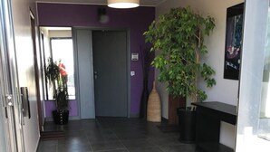 Un couloir avec un sol carrelé foncé, une porte et une plante en pot.
