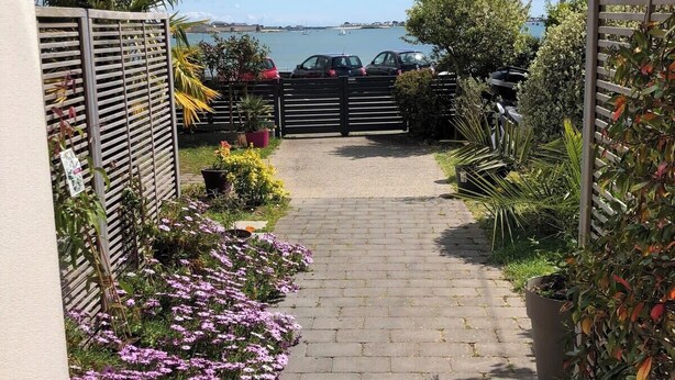 Un chemin pavé mène à un parking offrant une vue sur la mer et les bateaux.