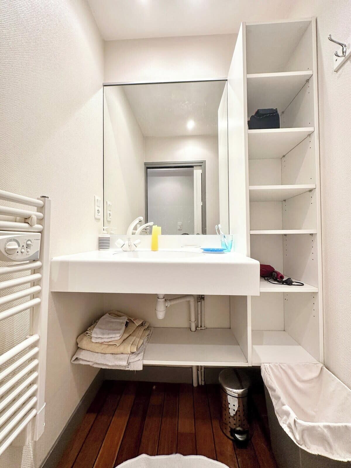 A modern bathroom with a white sink, mirror, and shelving unit.