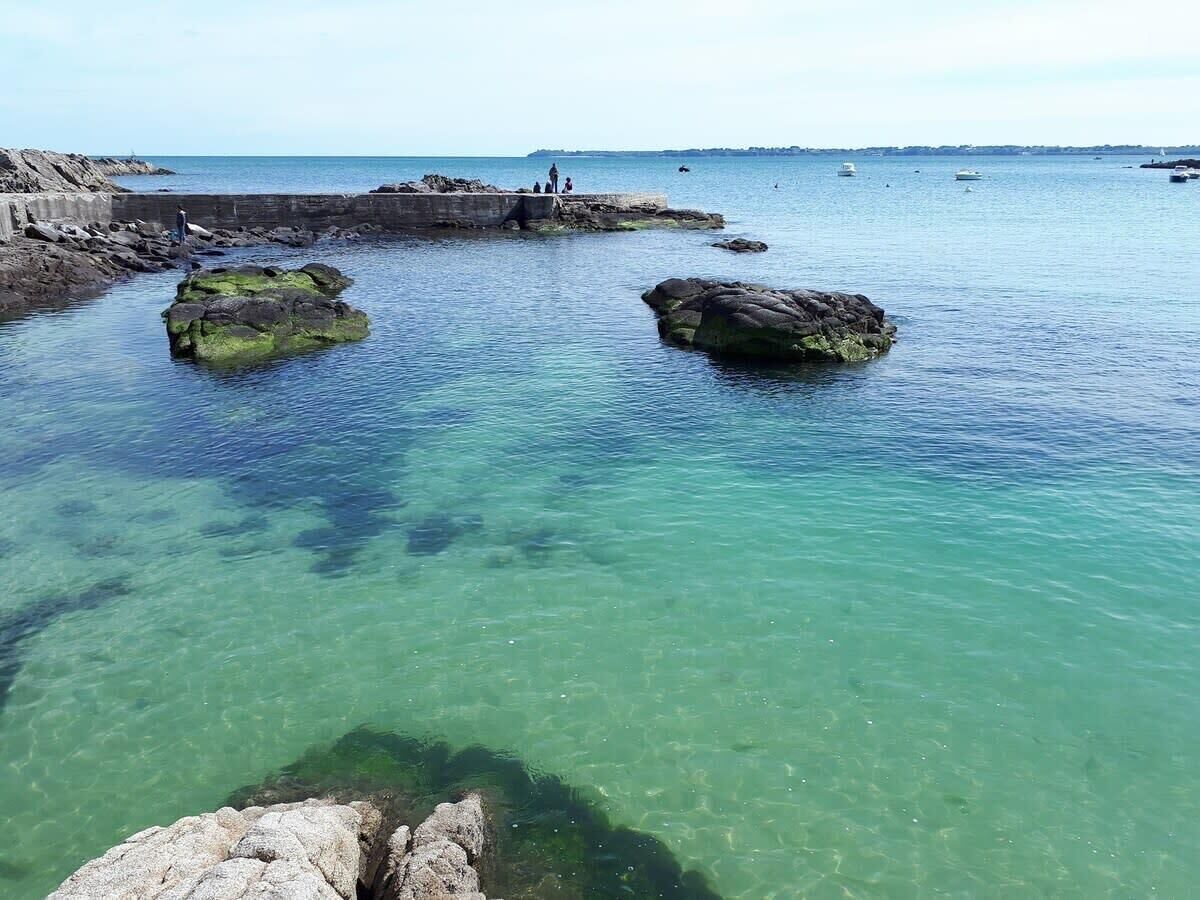 A coastal scene with clear water, rocky formations, and a pier with people.