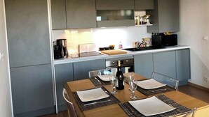 A modern kitchen with grey cabinets, a wooden dining table set with placemats and wine glasses, and a hanging pendant light.