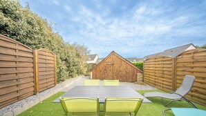 A patio with a table and chairs, a wooden fence, and a building in the background.