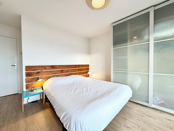A bedroom with a wooden headboard, a bed with white bedding, a nightstand, and a sliding glass door closet.