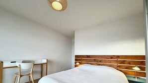 A bedroom with a wooden headboard, a bed with white bedding, a desk with a chair, and a bedside lamp. - T3 Standing Vue Mer 180° Face Plage (Larmor-Plage)