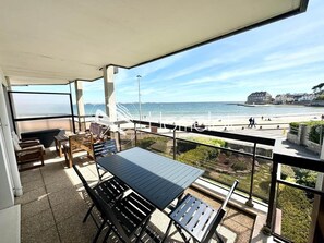 A balcony with a table and chairs, overlooking a beach and a coastal town.