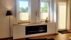 A room with two windows, a floor lamp, a vase with branches, a fruit bowl, and a mounted TV. - Vacation apartment Hovest - relaxation for up to 4 guests  (Ostbevern)