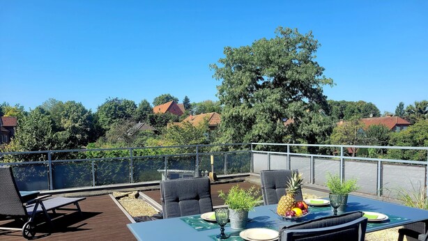 A rooftop terrace with a table set for dining, surrounded by chairs, and overlooking a scenic view of houses and trees. - Vacation apartment Hovest - relaxation for up to 4 guests  (Ostbevern)