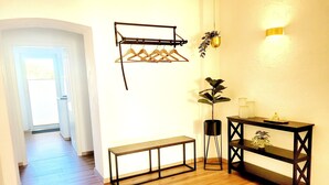 A room with a wooden floor, a round rug, a bench, a console table with shelves, a hanging plant, and a wall-mounted light fixture. - Vacation apartment Hovest - relaxation for up to 4 guests  (Ostbevern)