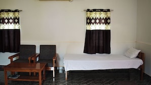 A room with a bed, two chairs, a small table, and an air conditioning unit on the wall. - Falcon Jungle Resort (Sarupeta)