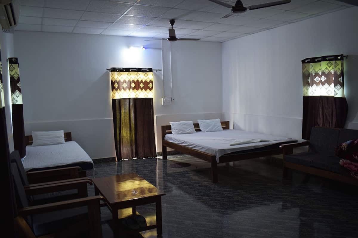 A hotel room with two single beds, a sofa, a table, and a ceiling fan.