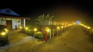 A nighttime view of a cobblestone pathway leading to a building with a thatched roof. - Falcon Jungle Resort (Sarupeta)