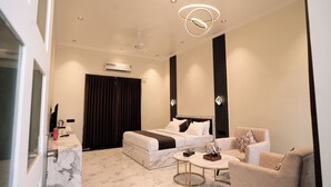 Una habitación de hotel moderna con cama, zona de estar, una mesita y un ventanal con cortinas.