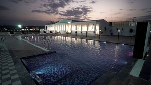 Una piscina con un borde de baldosas y sillones de descanso, rodeada por un edificio con ventanas de arco y techo de tejas.