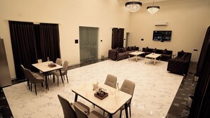 Habitación de hotel moderna con comedor, dos sofás, televisor y puerta de vidrio que da a un balcón.