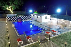 A swimming pool with a checkered pattern, lounge chairs, and a small building with a green sign. - Sukoon Farms (Jamwa Ramgarh)
