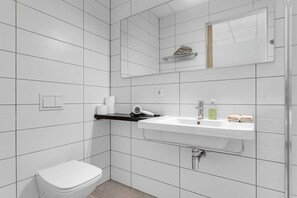 Un bagno moderno rivestito di piastrelle bianche, con lavandino bianco, water e porta asciugamani.