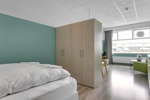 Una camera da letto moderna con un letto grande, un armadio, una scrivania e vista sulla città dalla finestra.