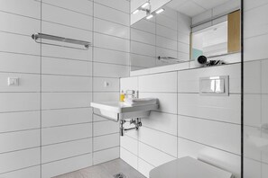 Casa de banho moderna com azulejos brancos, lavatório com toalha, espelho e barra de toalhas.