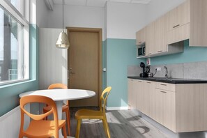 Uma cozinha moderna com uma mesa redonda e cadeiras, armários de madeira clara e uma janela que oferece luz natural.