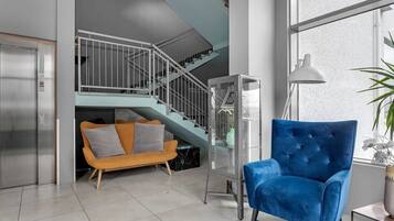 A modern living room with a blue armchair, a staircase, and a glass elevator.