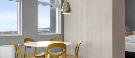 A modern room with a round table and yellow chairs, large windows, and a bed with white bedding.