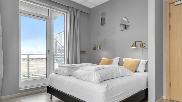Une chambre moderne avec un lit, une vue sur l’extérieur grâce à une grande fenêtre et un balcon.