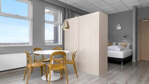 Une chambre moderne avec une table à manger ronde, quatre chaises, un lit et une grande fenêtre.