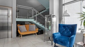 Un salon moderne avec un fauteuil bleu, un escalier et un ascenseur en verre.