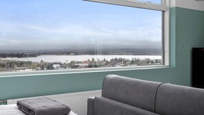 A room with a large window offering a view of a lake and distant buildings. - Icelandic Apartments - Beautiful Studio with view (Kópavogur)