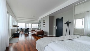 Un dormitorio amplio con una cama grande, un escritorio, una silla y un sofá. Hay un armario y un espejo en la pared.