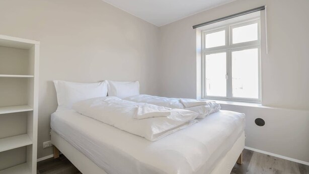 A bedroom with a bed, a window, and a white shelving unit.