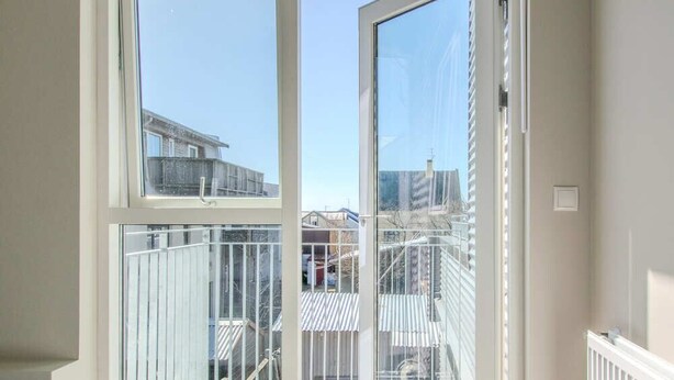 Un dormitorio con un ventanal grande, una cama y vistas a un balcón con barandilla.
