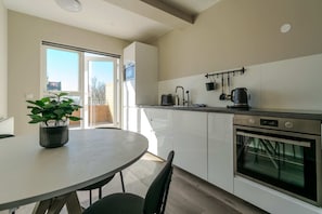 Una cocina moderna con armarios blancos, un horno de acero inoxidable y un comedor con mesa y sillas.