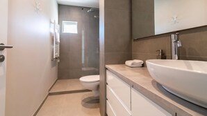 Un baño moderno con un lavamanos grande, inodoro y ducha.
