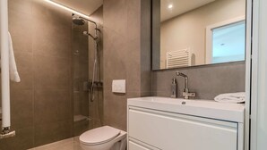 Un baño moderno con cabina de ducha de vidrio, inodoro blanco y tocador con espejo.