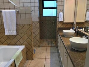 Bathroom features a walk-in shower, bathtub, and two sinks with faucets.