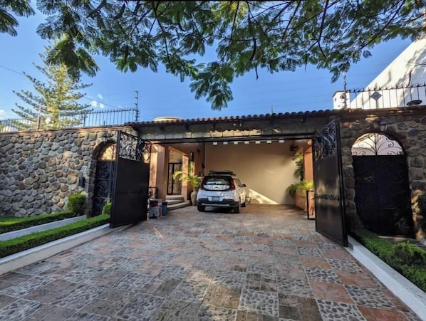 A stone-walled entrance with a tiled driveway leading to a covered parking area.