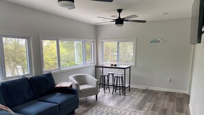 A modern living room with a blue sofa, a white armchair, and a small table. There are three windows providing natural light, and a ceiling fan is visible. - Hot Tub / Top 1% /  Kayaks /  950 Mbp /  Pets /  PickleB (Hot Springs)