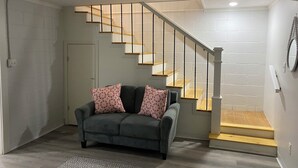 A living room with a grey sofa, two patterned cushions, a wooden staircase, and a white door. - Hot Tub / Top 1% /  Kayaks /  950 Mbp /  Pets /  PickleB (Hot Springs)