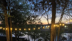 A gravel patio area with string lights, trees, and a view of a body of water and buildings in the background. - Hot Tub / Top 1% /  Kayaks /  950 Mbp /  Pets /  PickleB (Hot Springs)