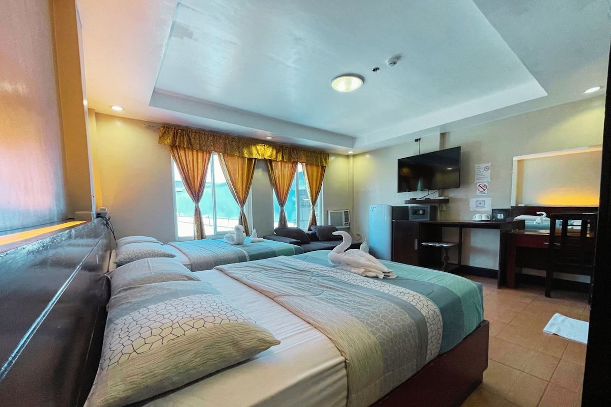 A hotel room with two beds, a desk, a TV, and a window with curtains.