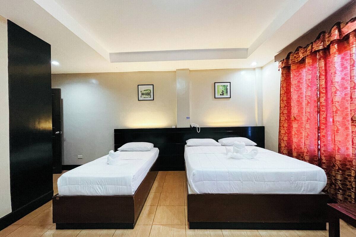 A hotel room with two single beds, a dark headboard, a large mirror, and a red curtain.