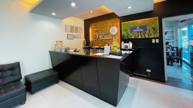A reception area with a black counter, a seating area with a bench, and a wall with certificates and a sign for 'Siayan Travellers Inn'. - Siayan Travellers Inn Manila powered by Cocotel (Pasay)