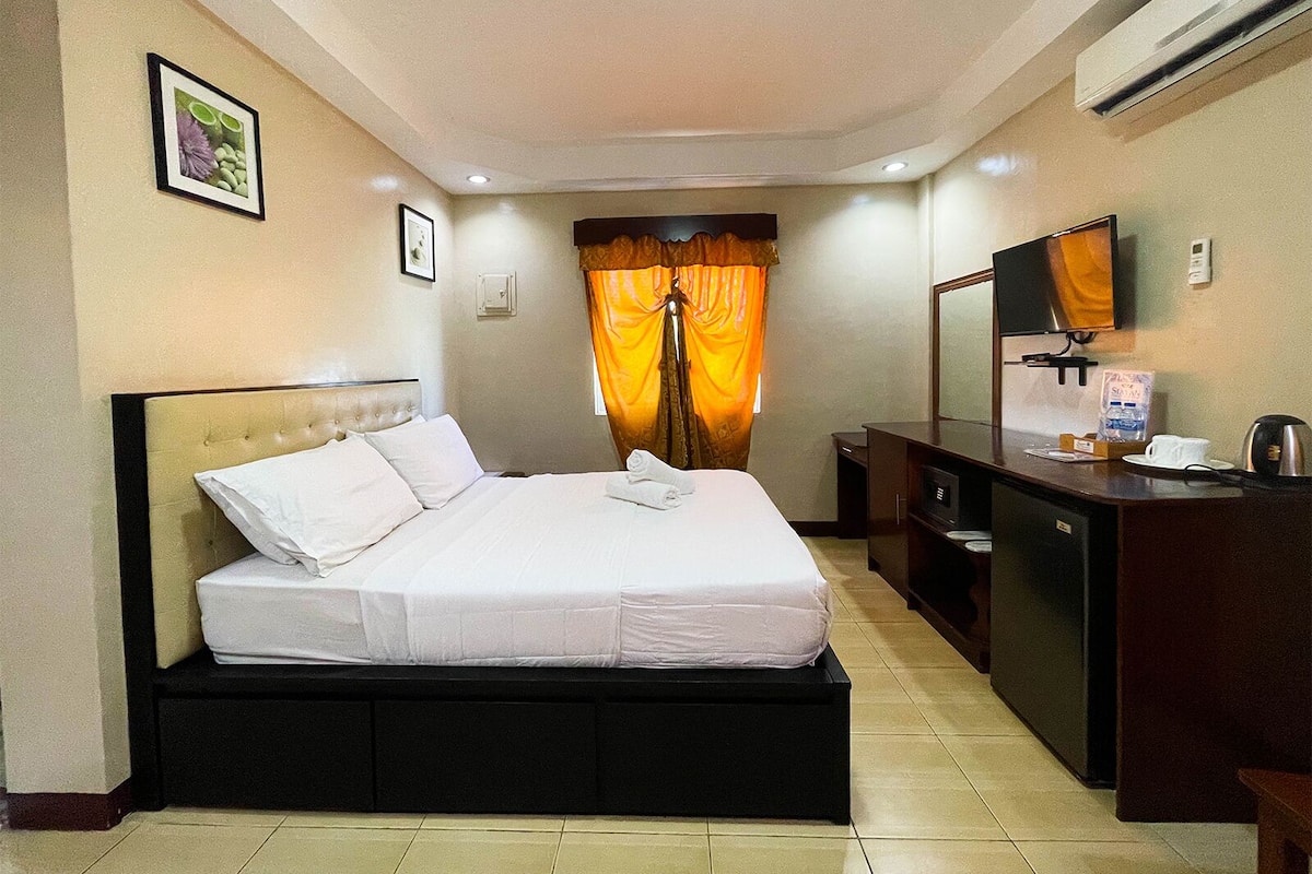 A hotel room with a bed, a desk, a television, and an air conditioning unit.