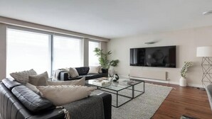 A modern living room with a black leather sofa, a glass coffee table, and a large flat-screen TV mounted on the wall.